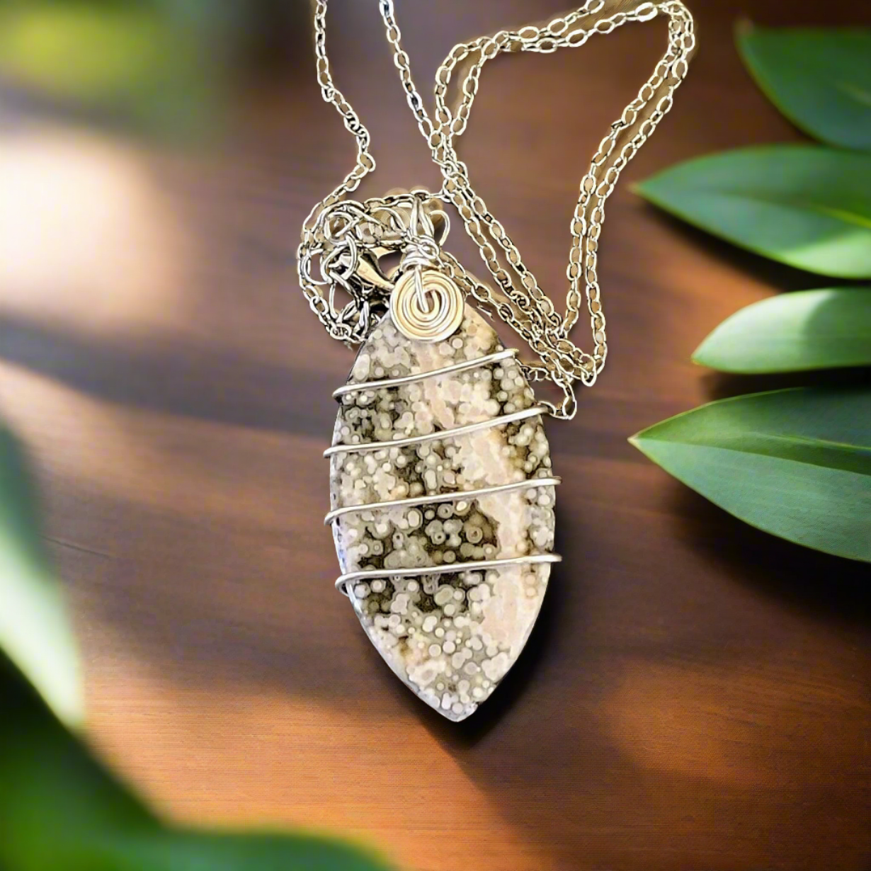 Green & White Ocean Geode Jasper Wire Wrapped Marquise Natural Stone Amulet Silver Necklace on wood table with leaves around the edges as decoration. 